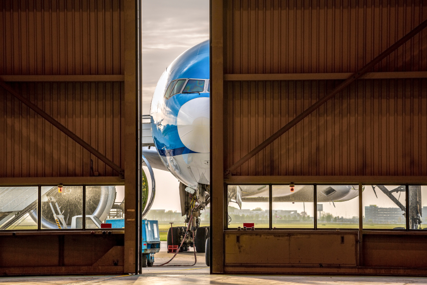 Airplane in front of half opened door to hangar